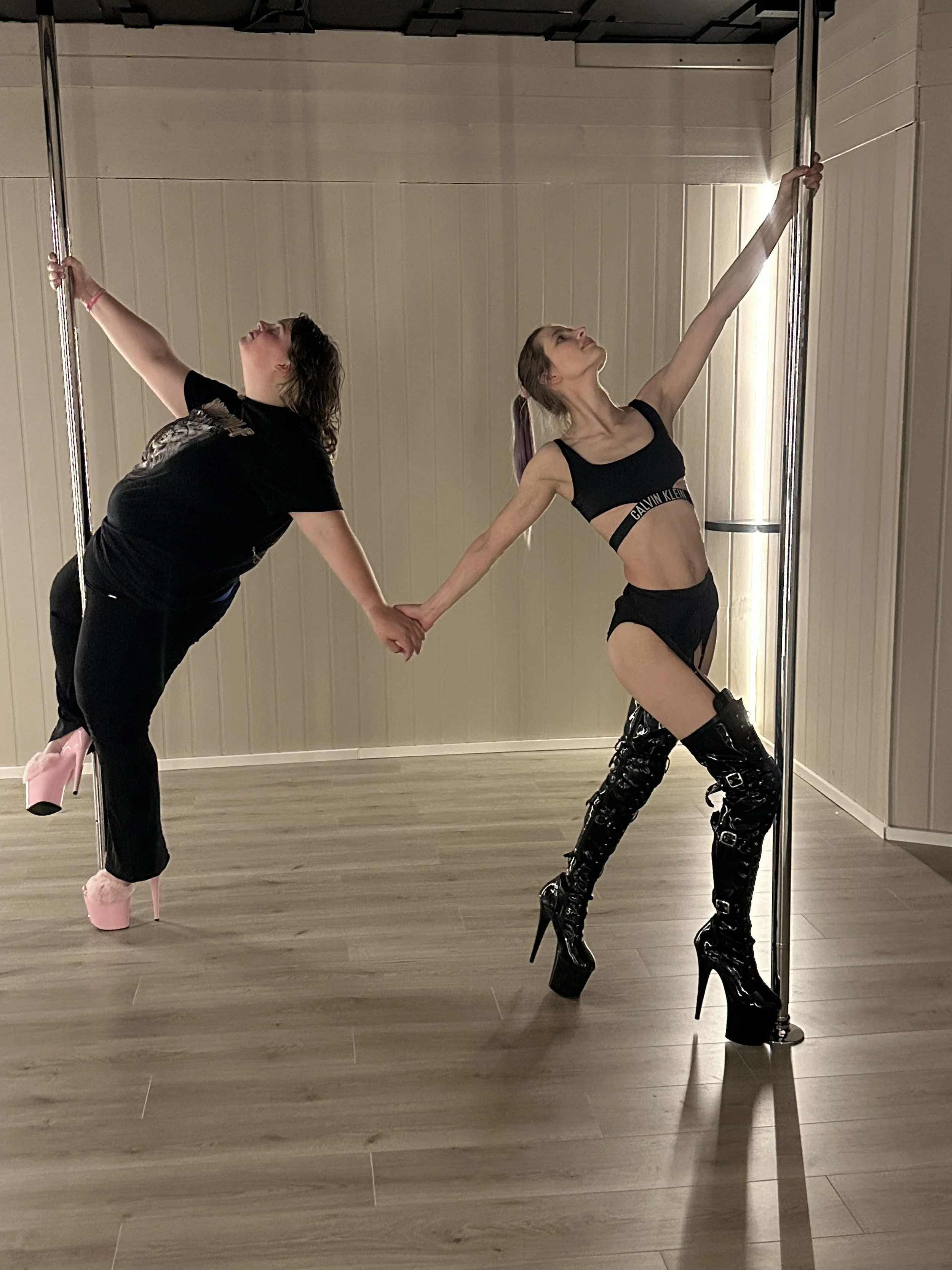 Two people holding a pole each, they stretch their arms out behind them and holds hands.