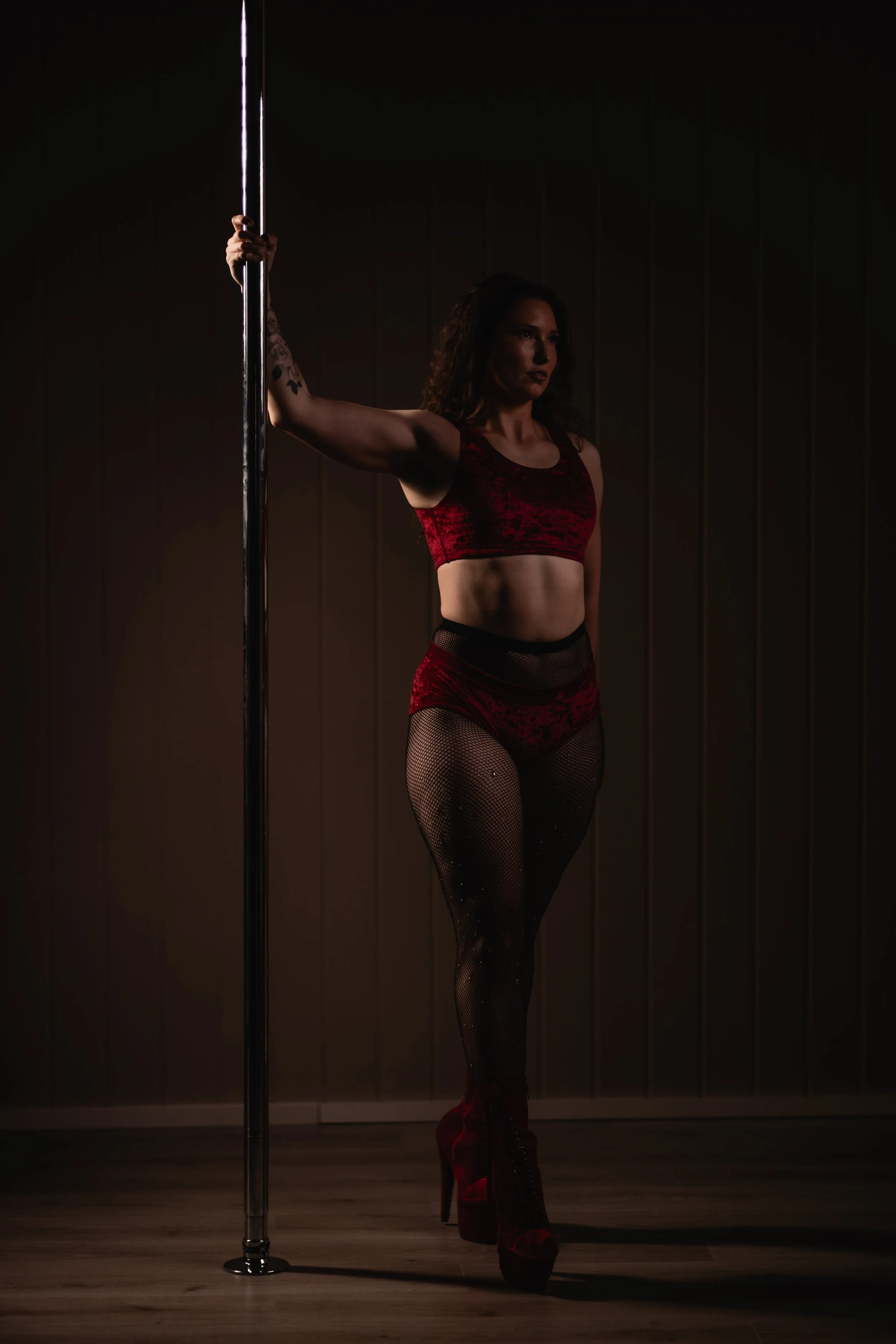 A pole dancer is standing beside the pole and holding onto the pole in a pose.
