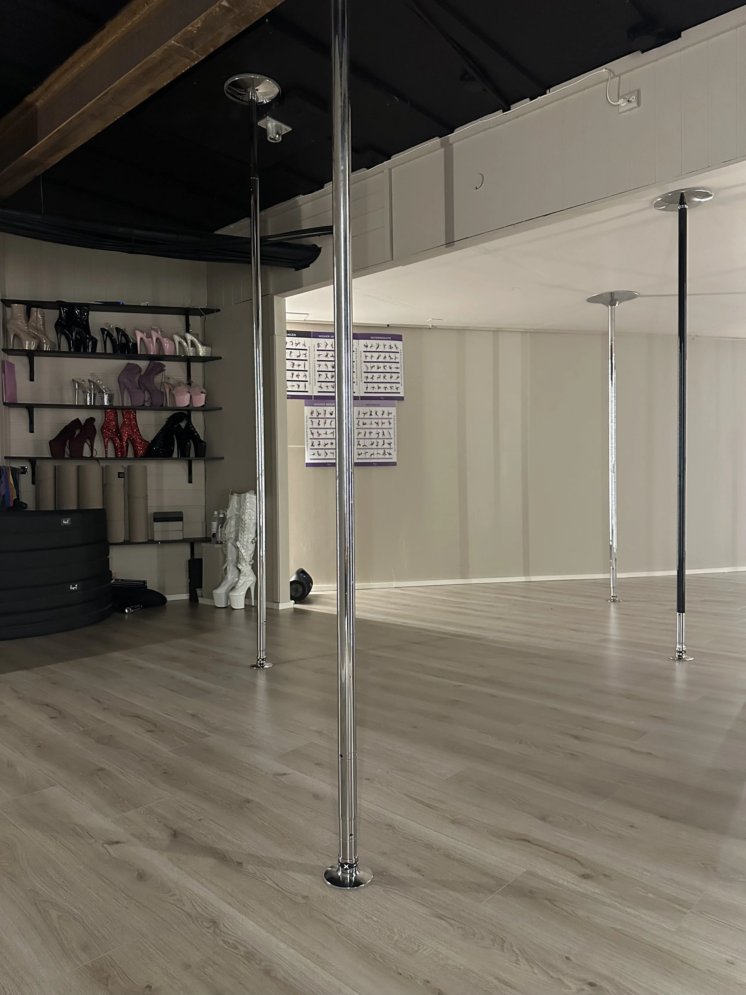 The pole studio. The image shows four poles and a rack of shoes on the back wall.