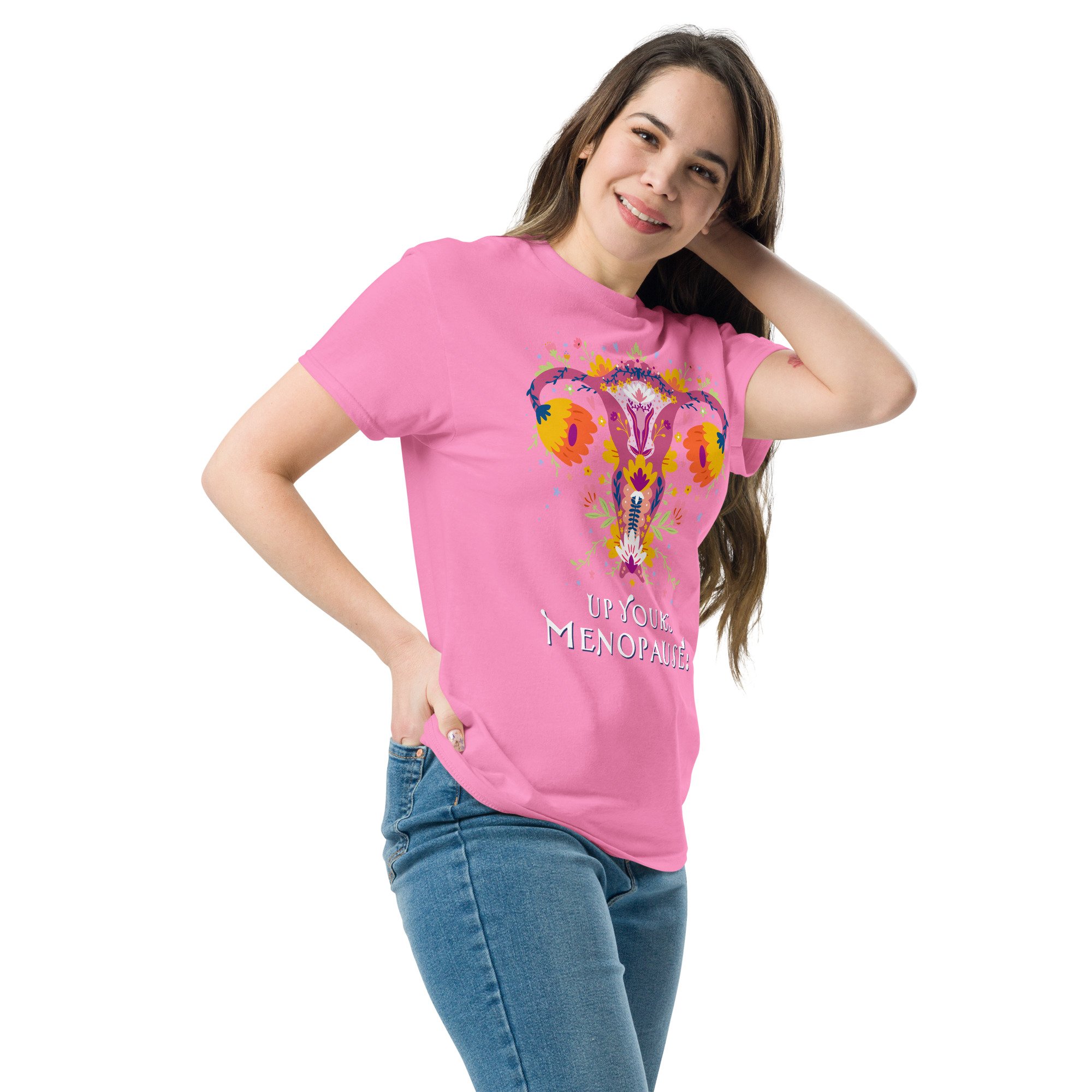 Young woman with long brown hair wearing a pink T-shirt with colorful graphic art and blue jeans, smiling, against a white background. Up Yours Menopause!' merchandise.