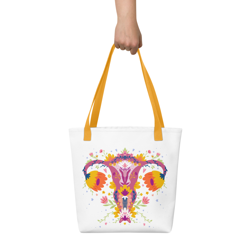 Person holding a white tote bag with brown handles featuring a colorful floral and uterus, lady bits and menopause sdesign. Up Yours Menopause!' merchandise.
