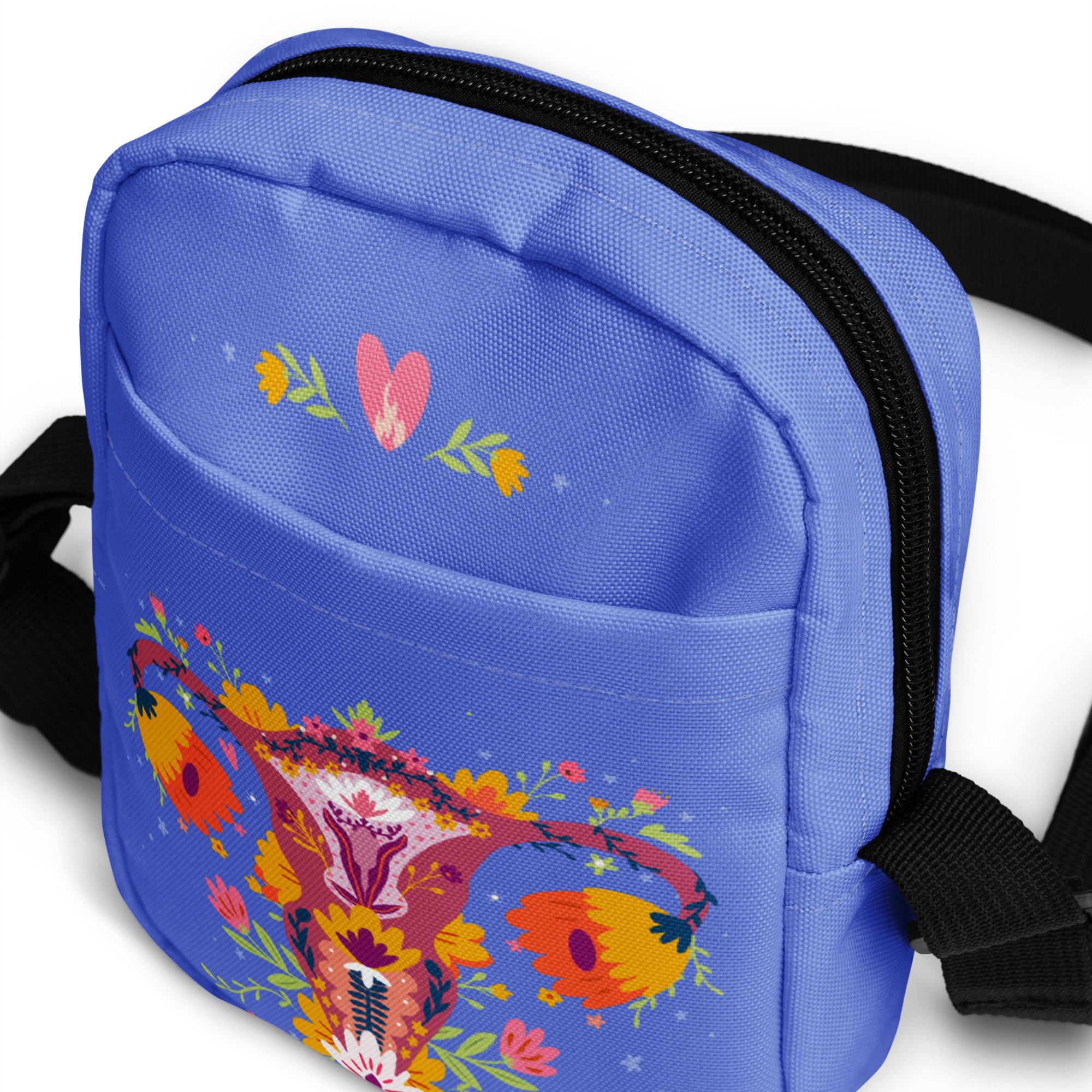 Close-up of a blue backpack with a colorful floral design, a black zipper, and a black shoulder strap. Up Yours Menopause!' merchandise.