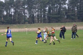 Girls playing rugby on a grassy field, with spectators watching