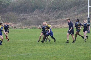 Youth rugby game featuring players in navy and yellow jerseys on a grassy field.