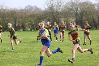 Children playing rugby on a grassy field.