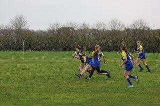 A group of young girls playing rugby on a grassy field, with some girls running and chasing the ball.