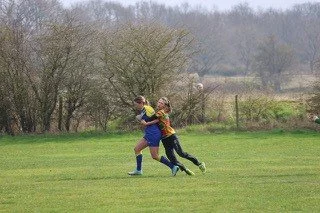 Two children playing chase on a grassy field with trees in the background.