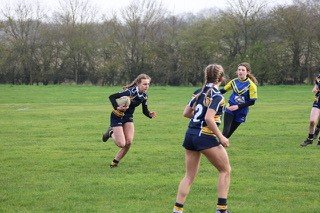 Girls playing rugby outdoors on a grassy field