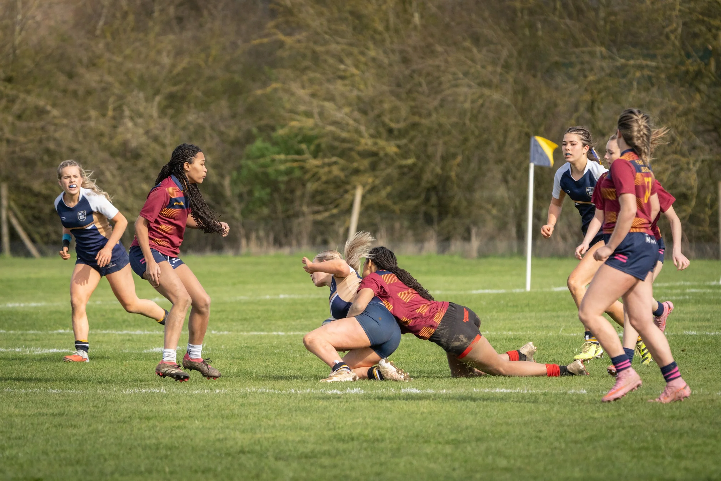 Women playing rugby on a grassy field with trees in the background during daytime.