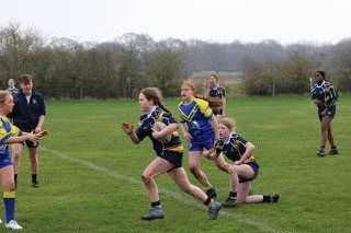 Children playing rugby on a grassy field.