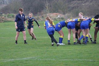 Women’s rugby match with players engaging in a scrum on a grassy field