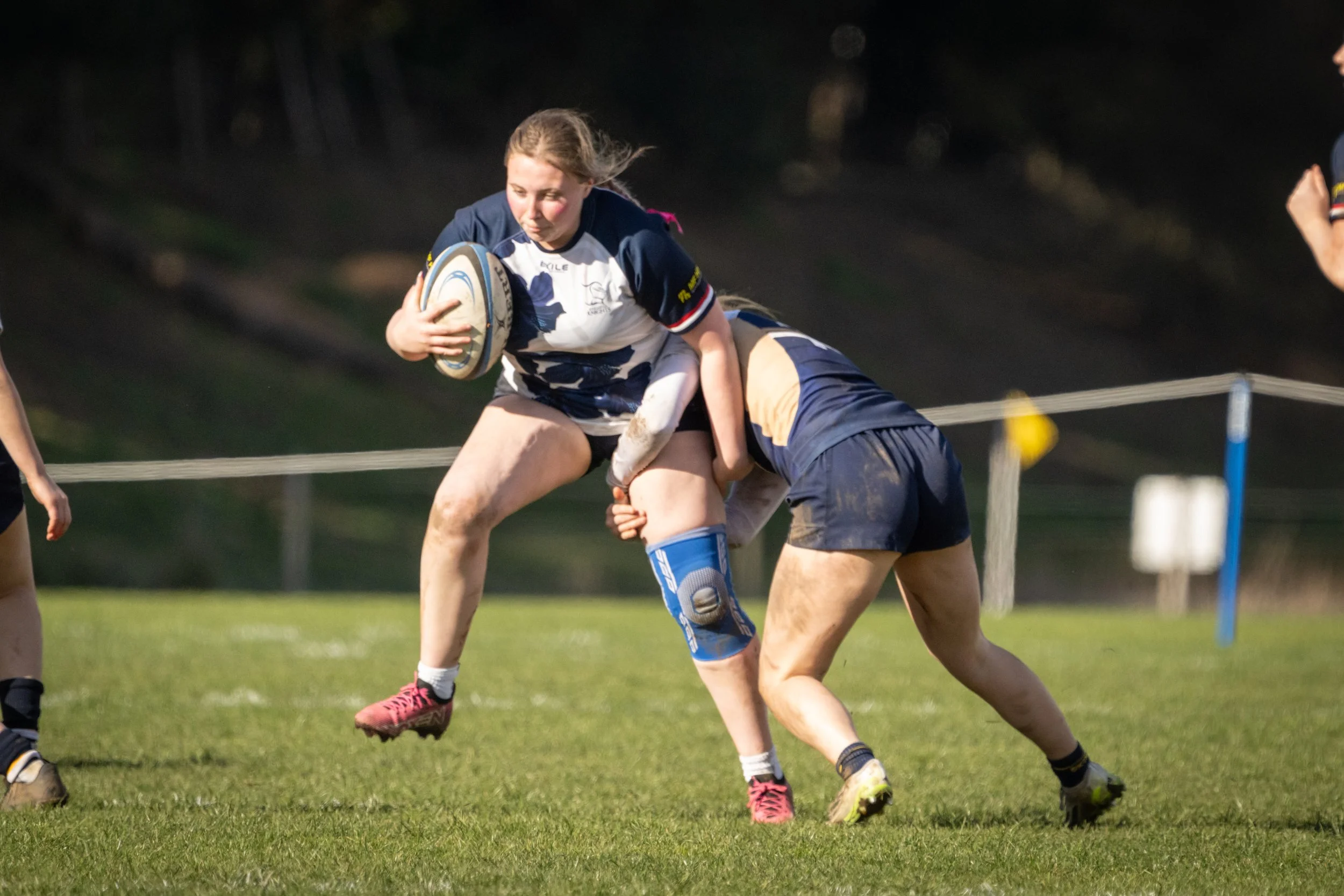 Girl in rugby uniform holding a rugby ball during a match on grass field.