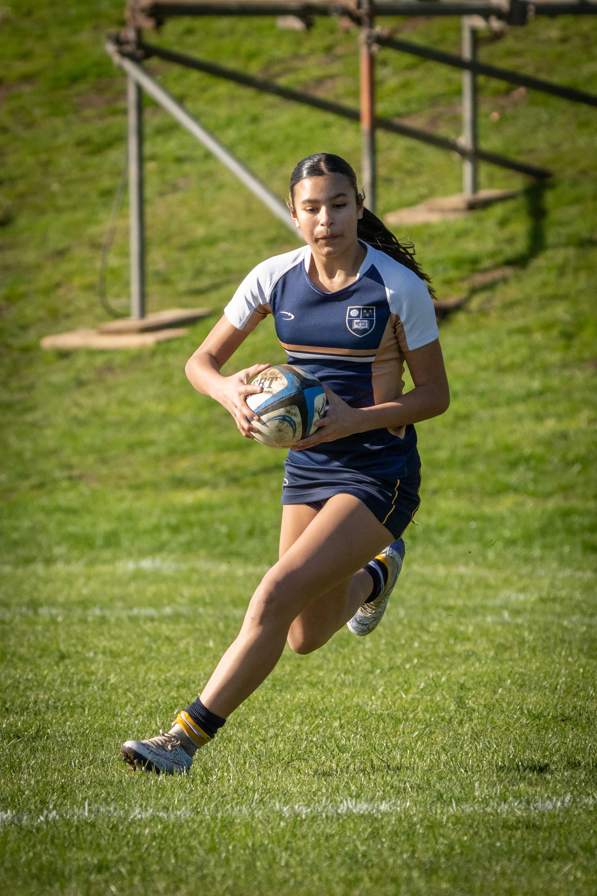 A girl running on a grassy field while holding a rugby ball.