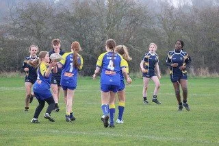 A group of female rugby players in blue and black uniforms playing on a grassy field.
