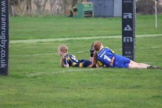 Two young children lying on grass near rugby goalpost, one resting and one looking away