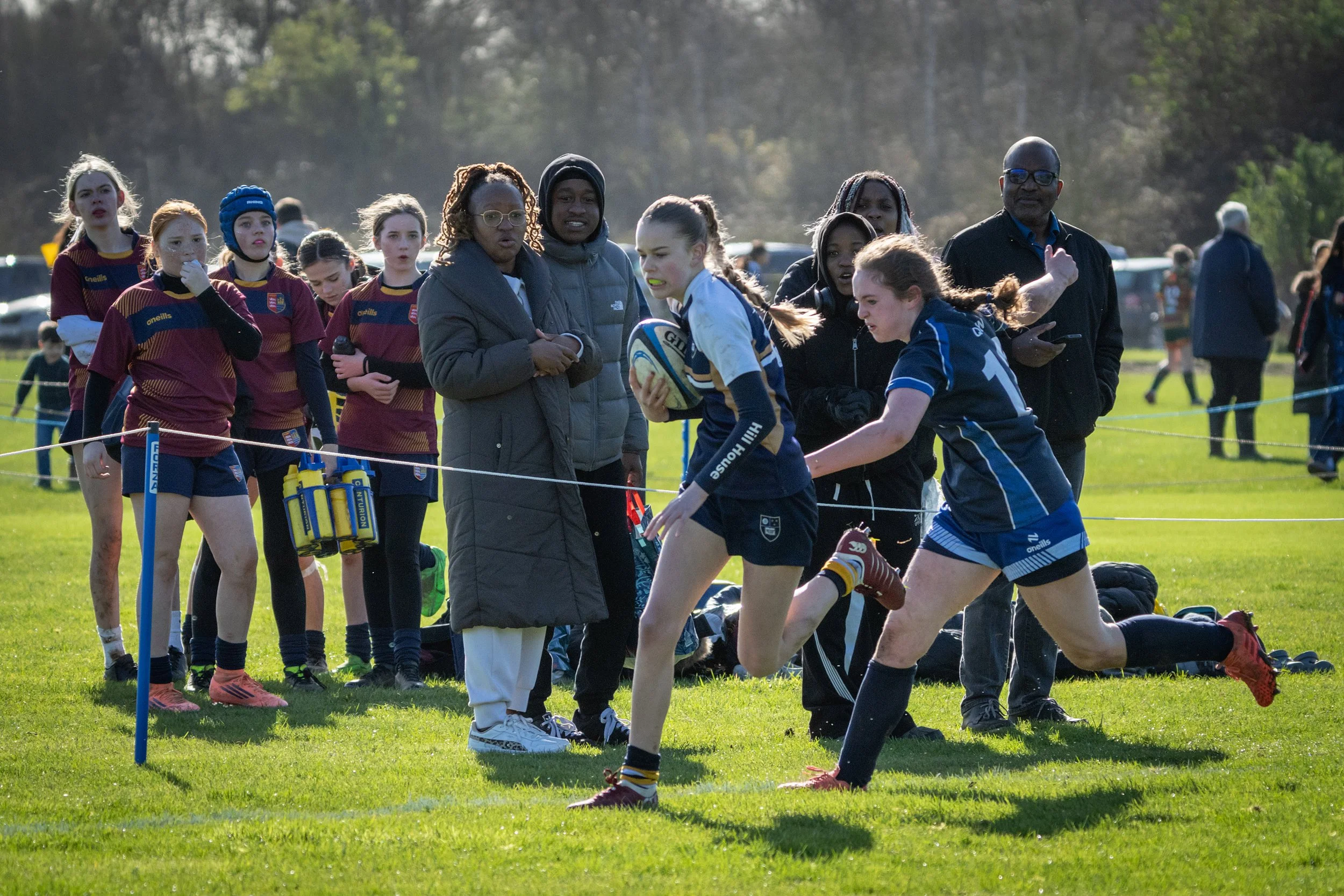 Girls rugby team on the field with coaches during a match.