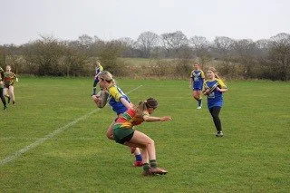 A rugby game with players competing on a grassy field, some are attempting to catch or tackle the ball.