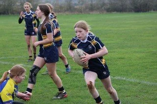A group of young girls playing rugby outdoors on a grassy field.