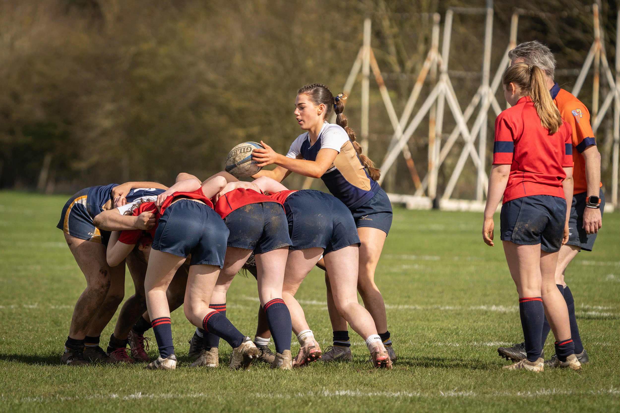 Girls playing rugby on a field with referees, engaged in a line-out during a match.