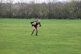 A person in athletic clothing holding a rugby ball, standing in a grassy field during daytime.
