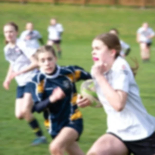 Children playing rugby on a grassy field.
