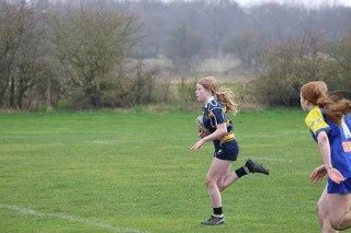 Two young girls running on a grassy field during a sports activity.