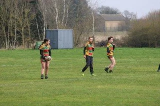 Three women in rugby uniforms walking across a grassy field.