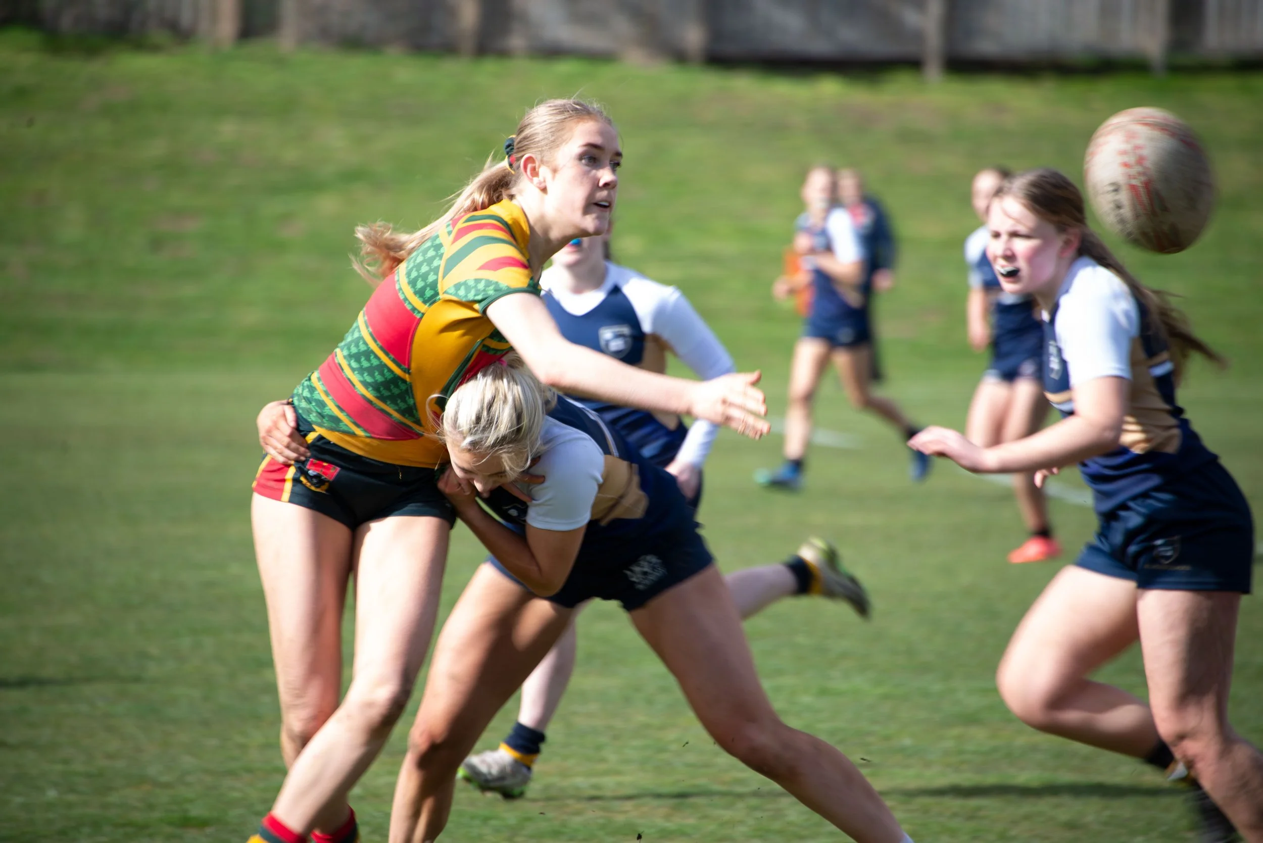 Women's rugby game on the field with players engaging in tackle and pursuit.