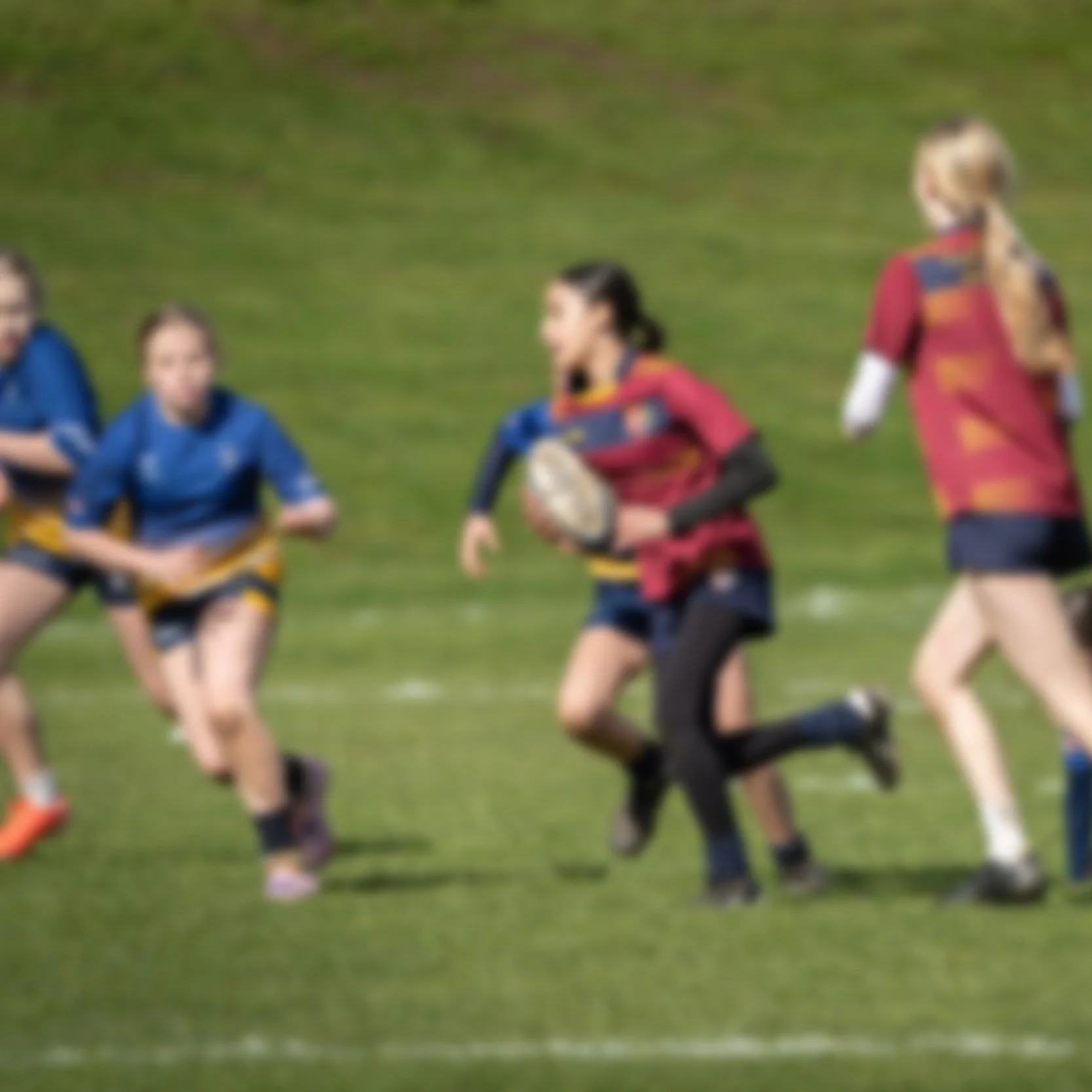 A Photo of a girls' rugby game with players in red and blue jerseys on a grassy field.