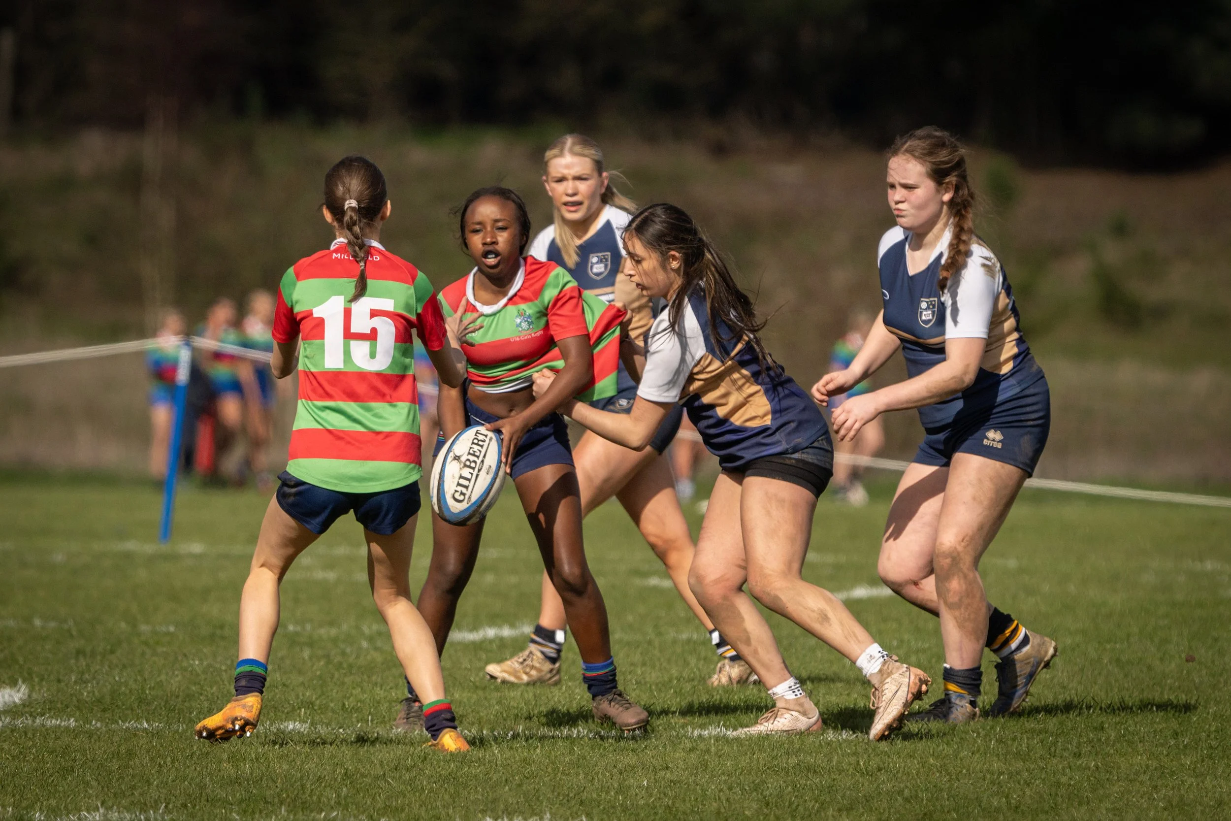 Girls playing rugby on a grassy field, wearing colorful uniforms and tackling each other during a game.