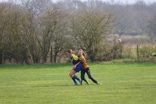 Two children playing rugby on a grassy field with trees in the background.