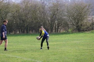 Two children playing rugby on a grassy field with trees in the background.