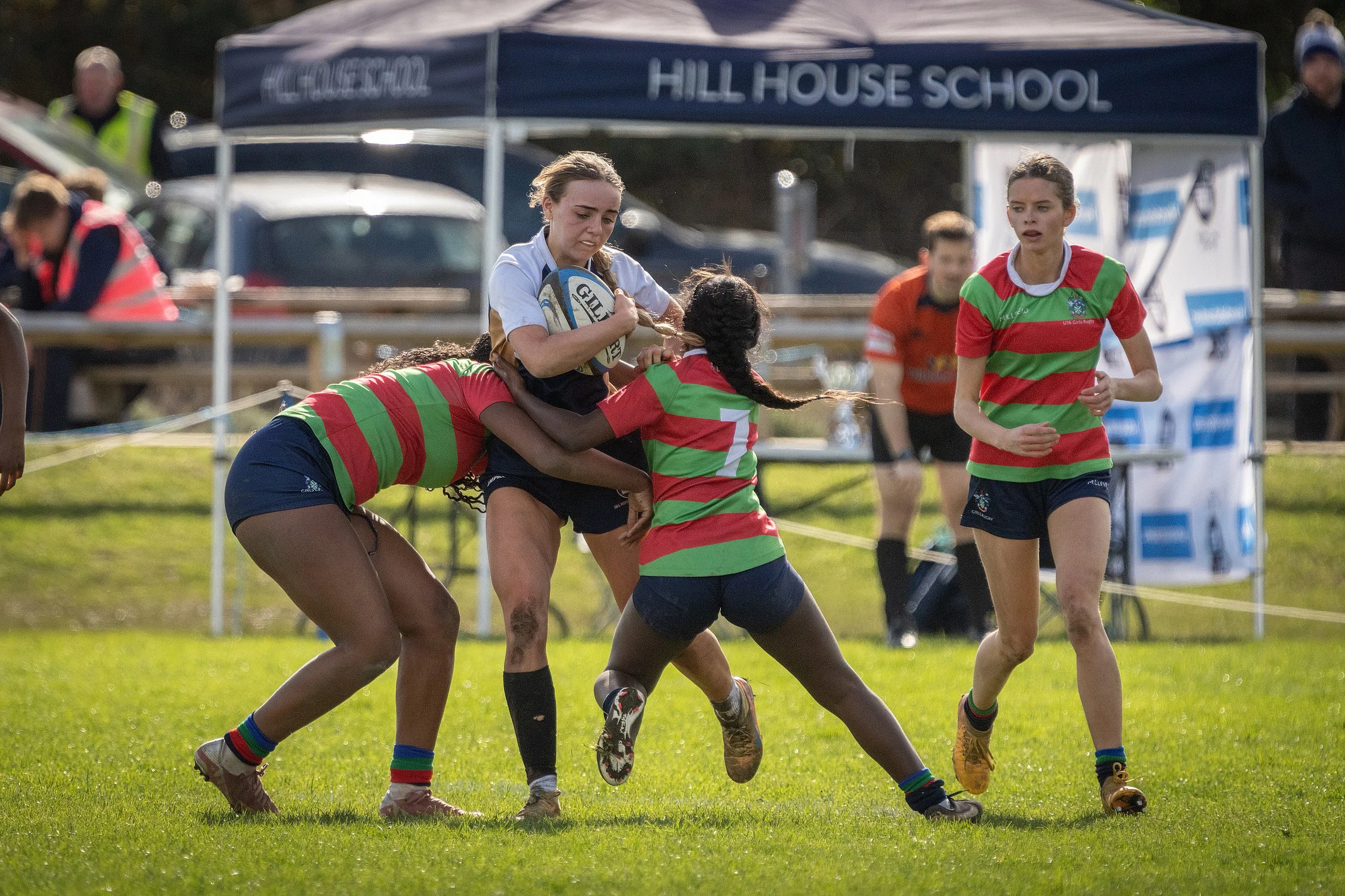 Girls playing rugby on a grassy field with a blue tent that has 