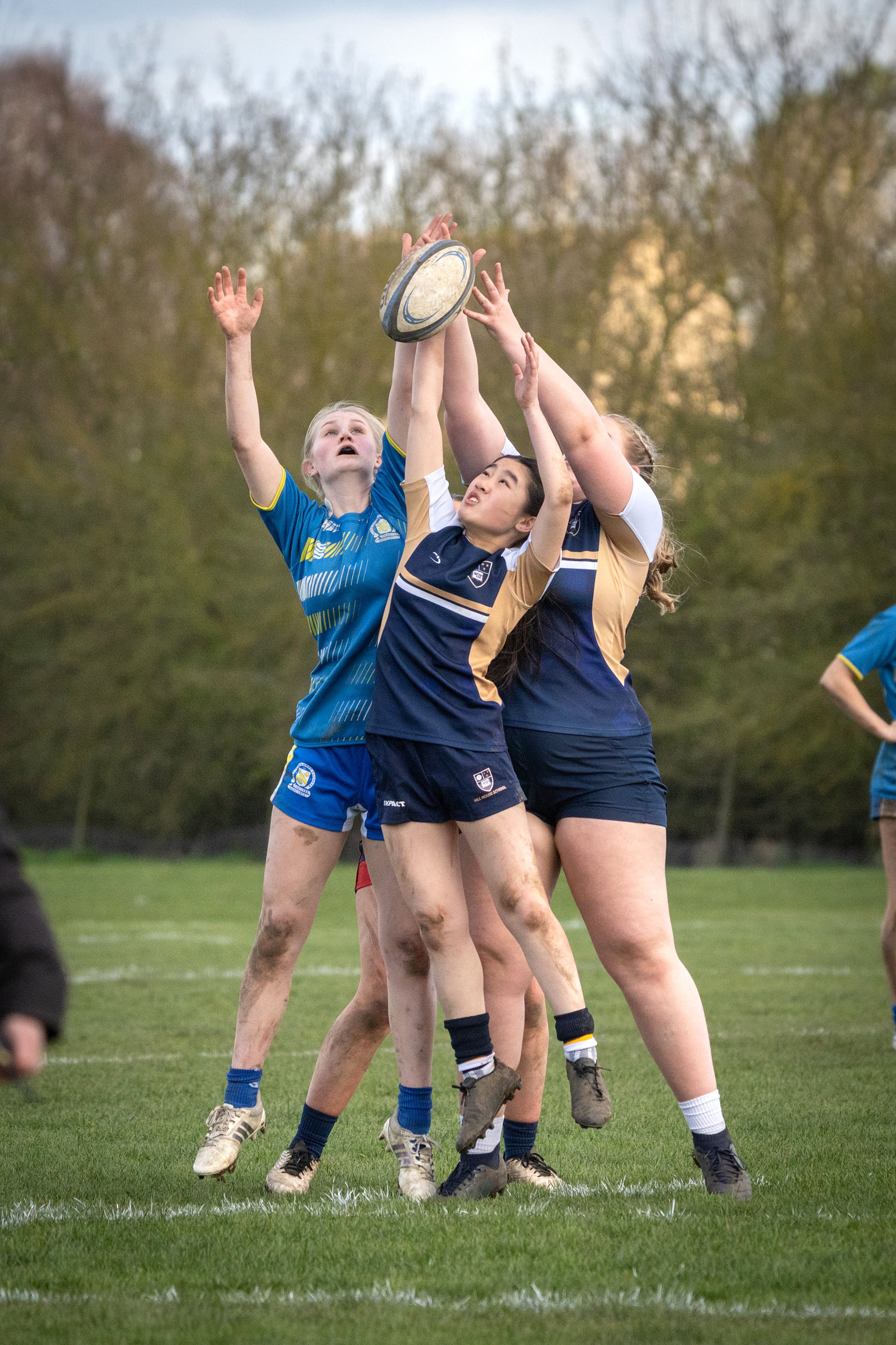 A group of women playing rugby on a field during a match, reaching for a rugby ball in mid-air.