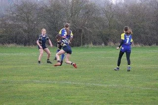 Children playing flag football on a grassy field with trees in the background.