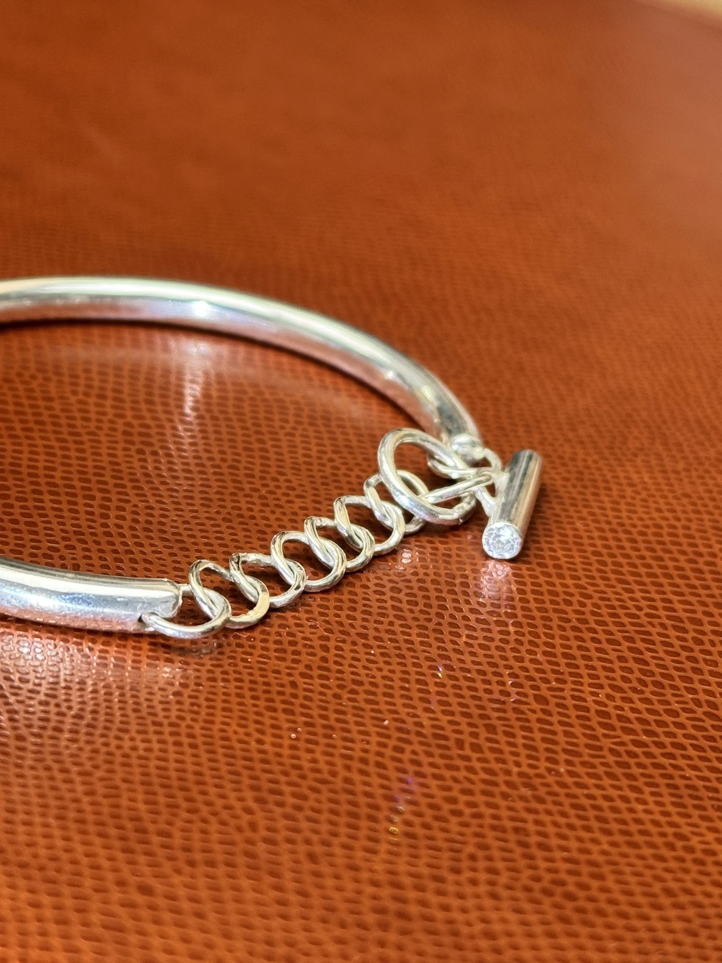 Une bracelet en argent avec un petit diamant posé sur un fond en cuir orange.