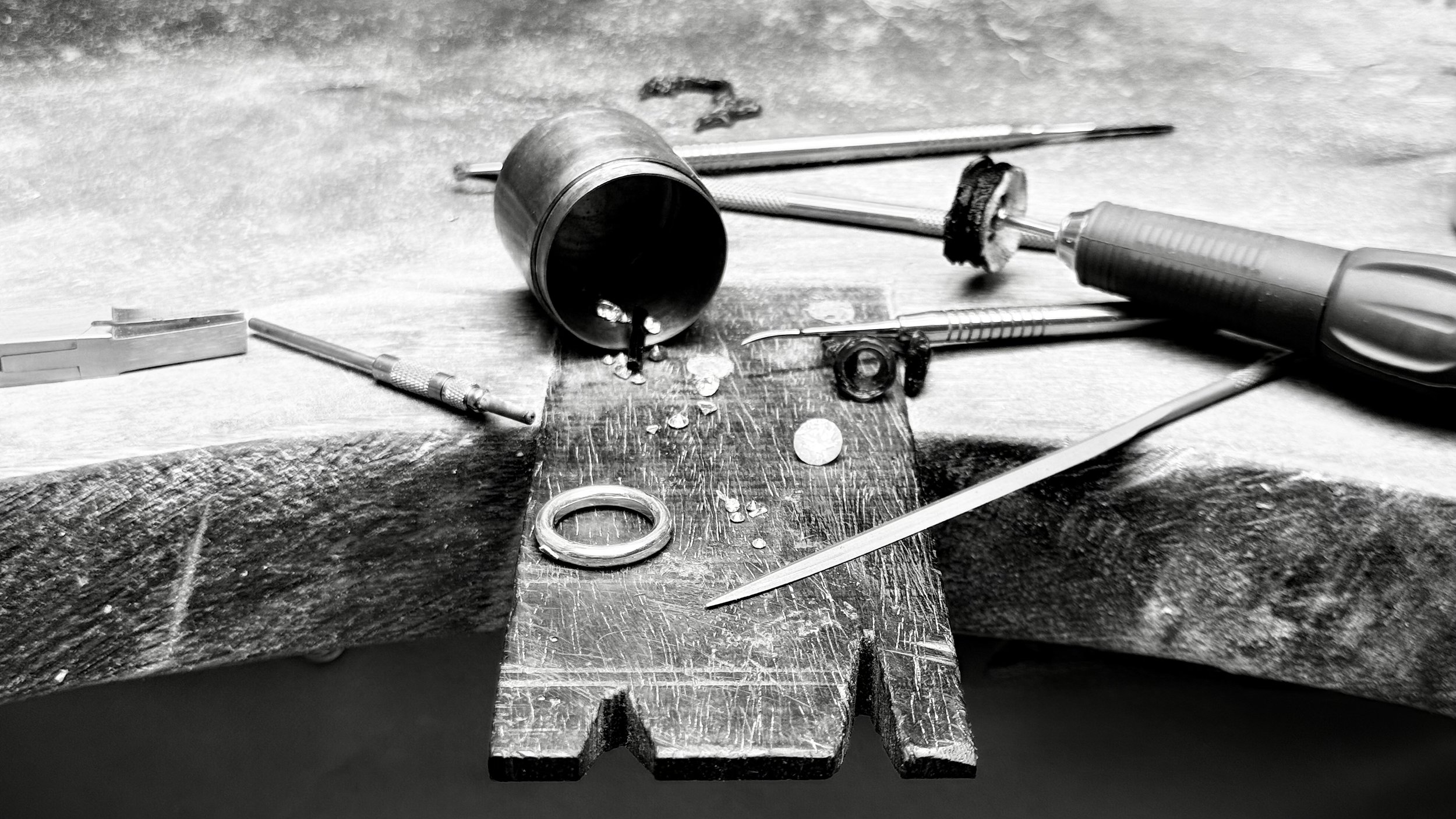 Outils de réparation, notamment une lime, une pince, une pièce a main, des pierres et un bijou, disposés sur une surface de travail en bois appelée cheville .
