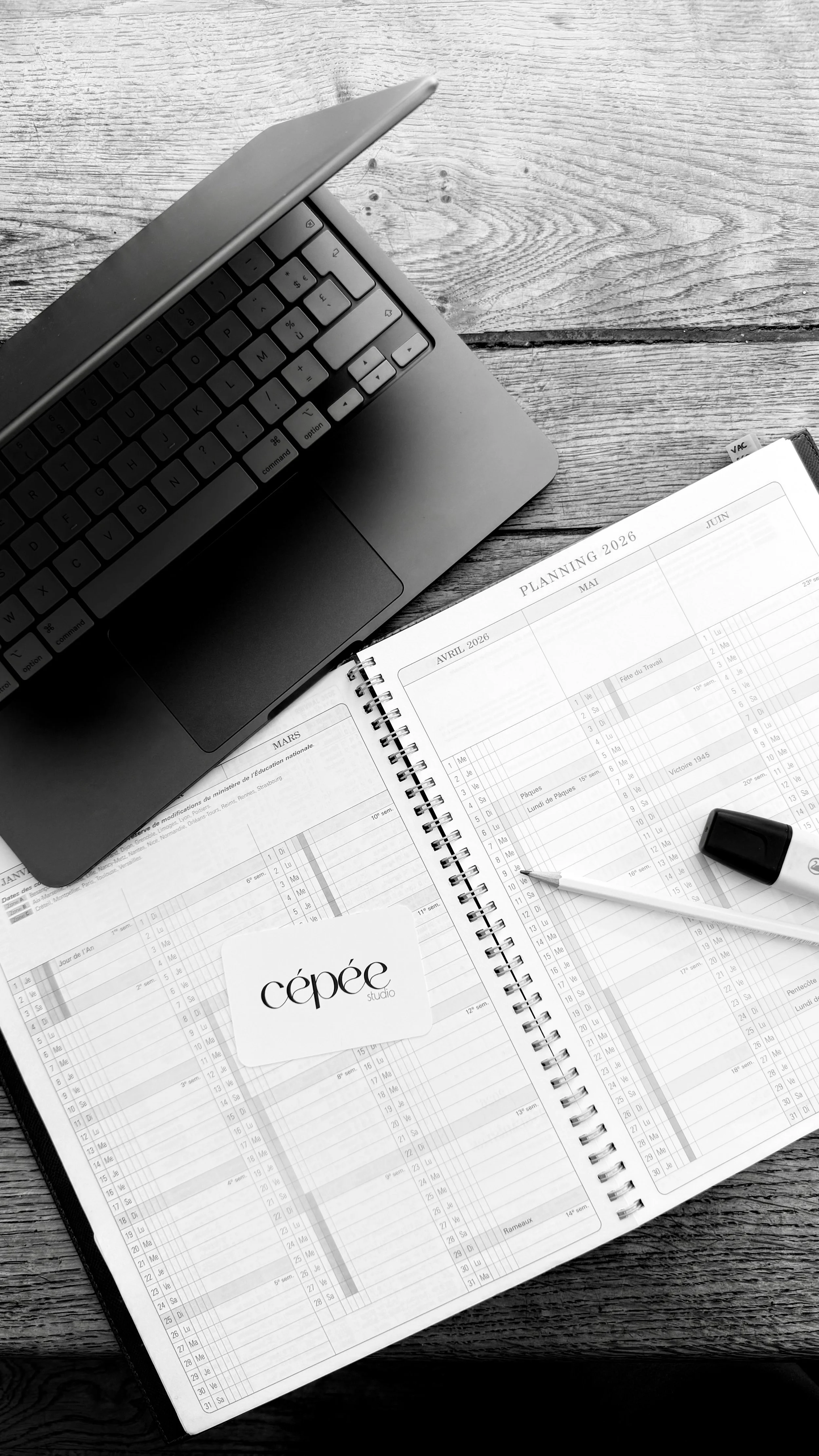 Agenda de planification annuelle ouverte avec calendrier, stylo, gomme, calepin, et un ordinateur portable sur une surface en bois.