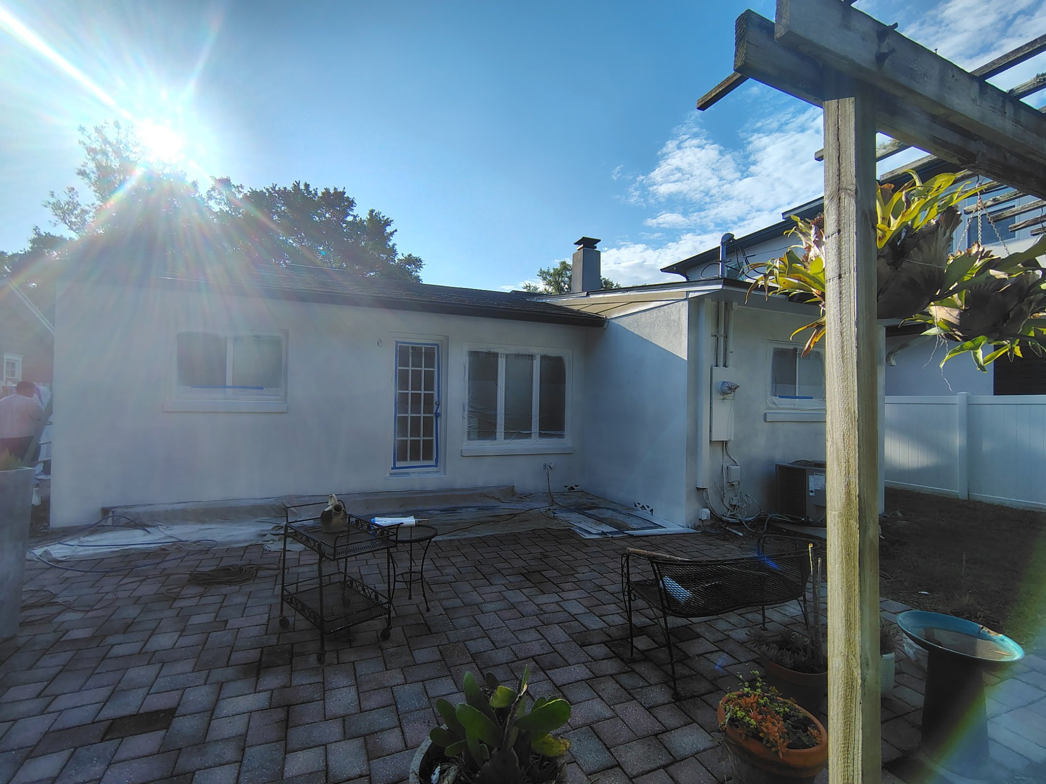 This image shows the patio and rear exterior of a Winter Park, FL home during the stucco painting process. Coats of Quality Painting protected the patio, masked windows and doors, and prepared the home for a clean Sherwin-Williams exterior paint fini