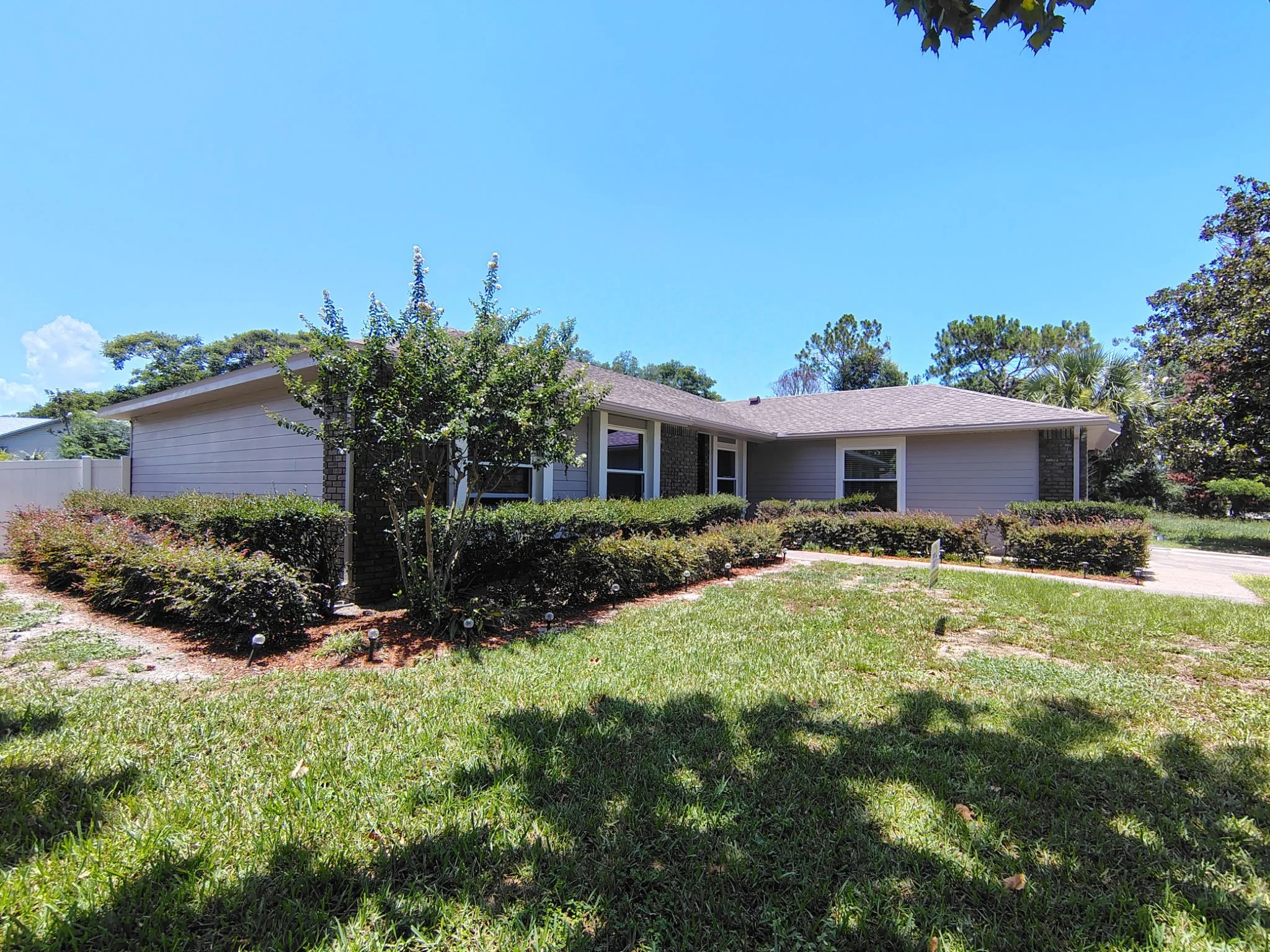 Front walkway view of an Ocoee home after exterior painting, showing modern gray siding, bright white window and roofline details, original dark brick, landscaping, and a Coats of Quality Painting sign.