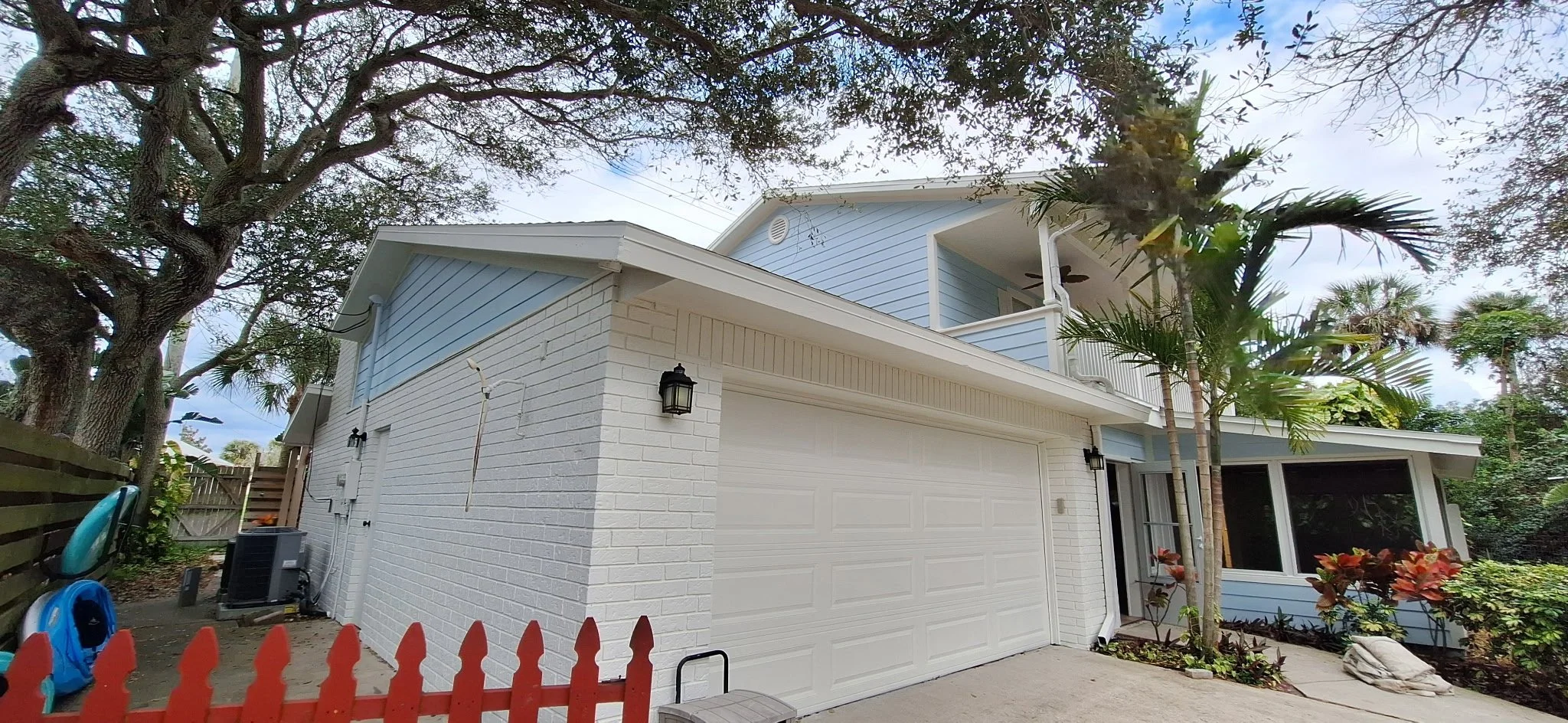 Wide exterior view showcasing white painted brick, coastal siding, and lush landscaping in New Smyrna Beach, Florida.