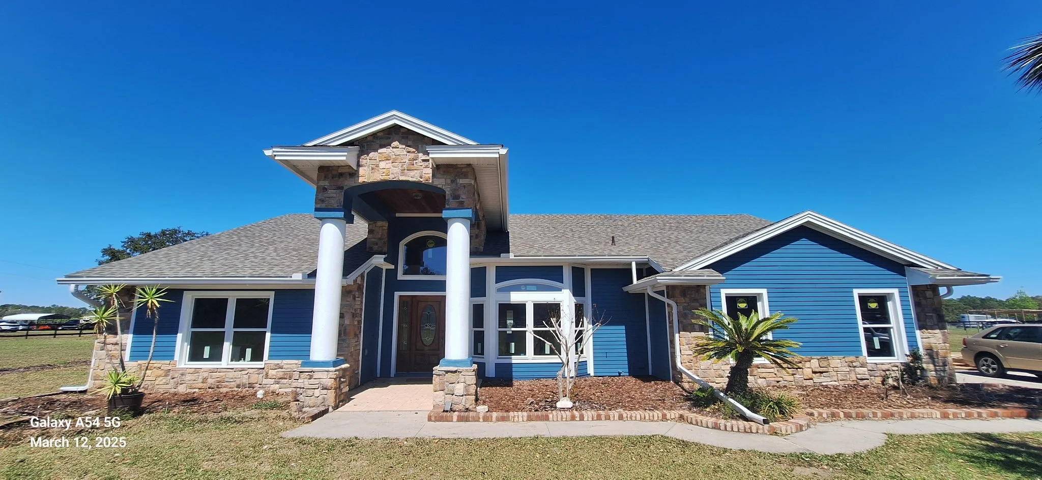 Exterior house painting project in Ocala Florida featuring modern blue siding, white trim, and stone column entrance by Coats of Quality Painting