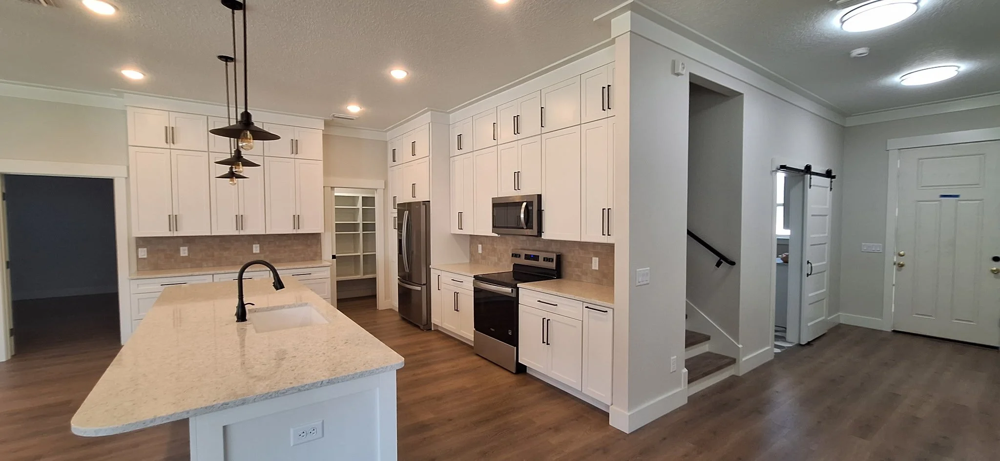 Modern kitchen with white cabinets, stainless steel appliances, a large beige island with a black faucet, and hardwood floors.