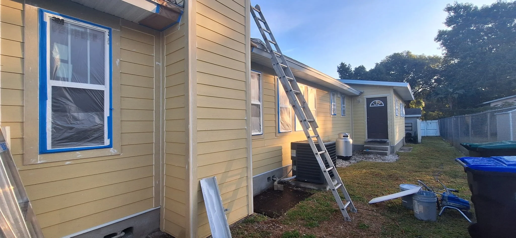This image captures the exterior house painting process in Orlando, FL, featuring detailed masking, window protection, and surface preparation. Coats of Quality Painting, LLC provides professional exterior painting services in Orlando and surrounding