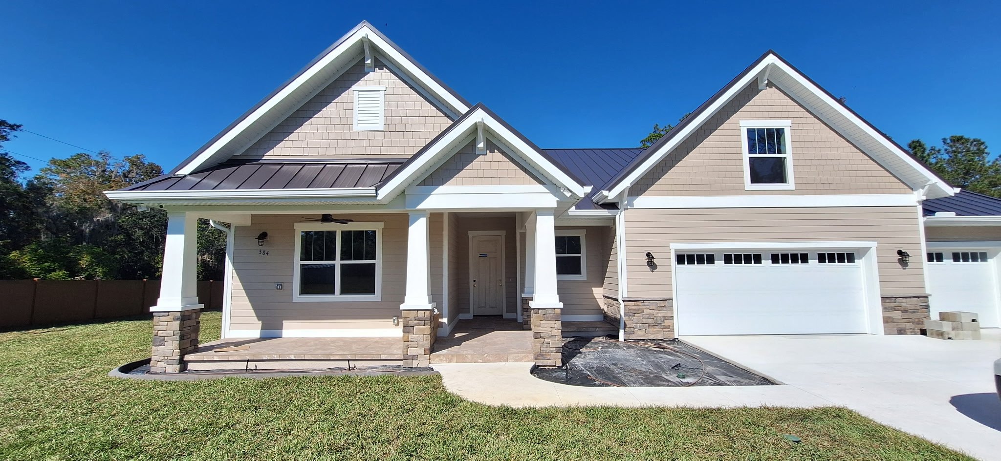 Freshly painted new construction home exterior in Sanford, Florida with tan siding, white trim, and stone columns by Coats of Quality Painting.