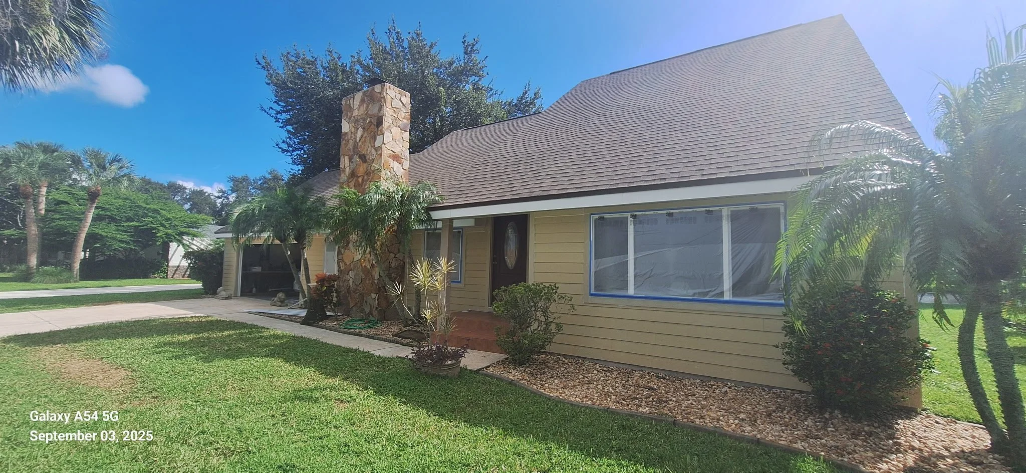 Before exterior painting of Melbourne FL Hardie Board home showing faded yellow siding and preparation by Coats of Quality Painting.
