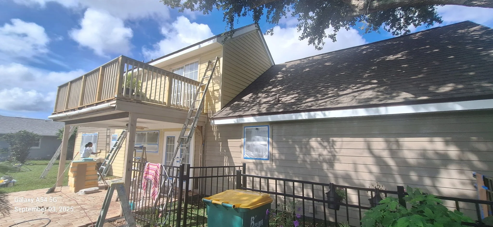 Before exterior painting of Melbourne FL Hardie Board home showing faded yellow siding and preparation by Coats of Quality Painting.