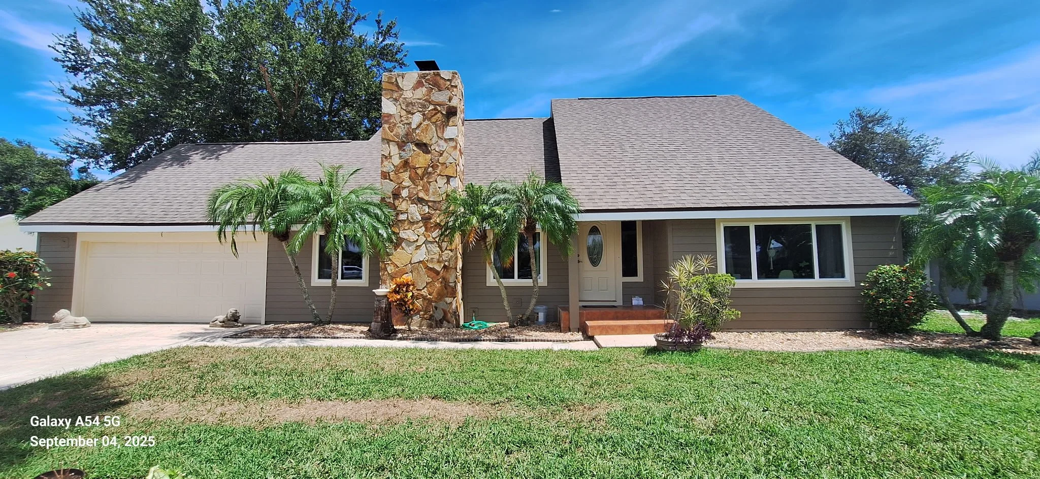 After exterior house painting in Melbourne FL showing taupe Hardie Board siding with white trim and stone accent chimney, completed by Coats of Quality Painting.