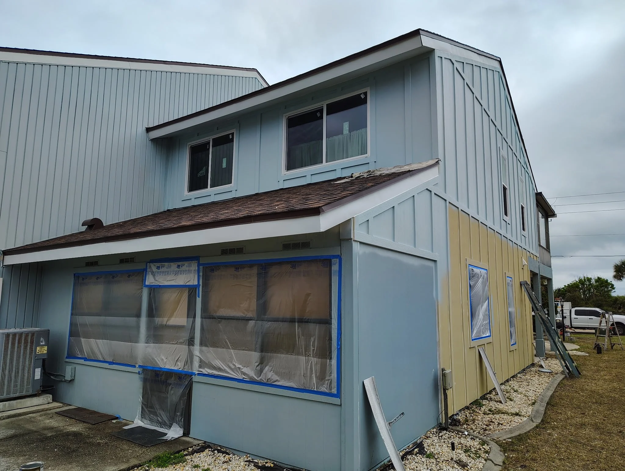 Side view of South Daytona home during exterior painting with masked windows and fresh blue paint