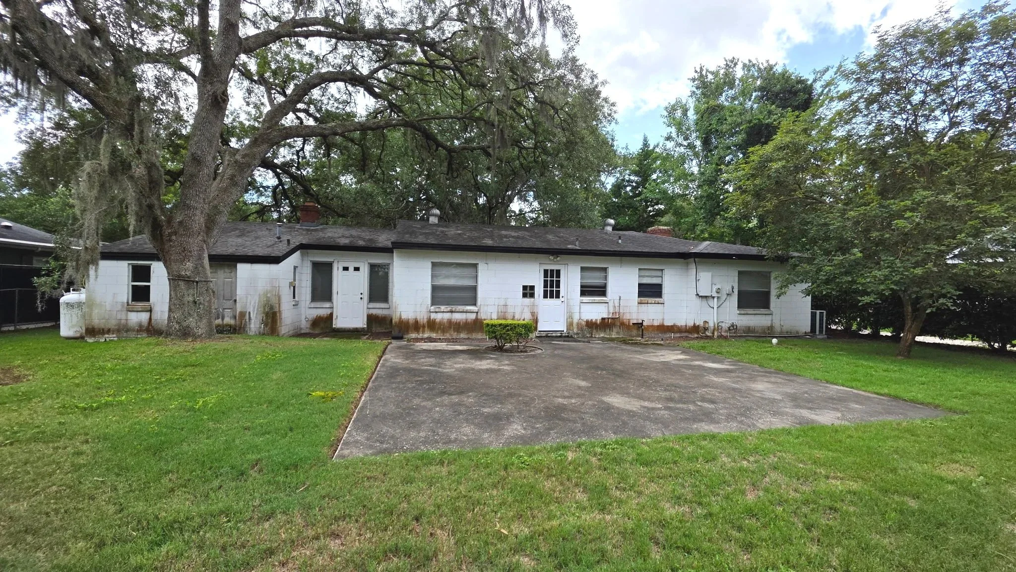 Before exterior painting photo showing heavy brown staining and discoloration on the rear white concrete block walls of a Winter Park home.
